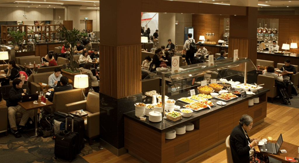공항 라운지 내부, 뷔페 스타일 음식과 음료, 여행객이 노트북으로 작업하며 휴식하는 장면